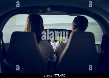 Rear view of male pilot giving training to trainee in flight simulator Stock Photo