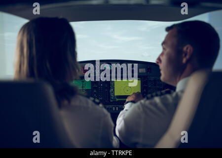 Rear view of pilot giving training to male trainee in flight simulator Stock Photo