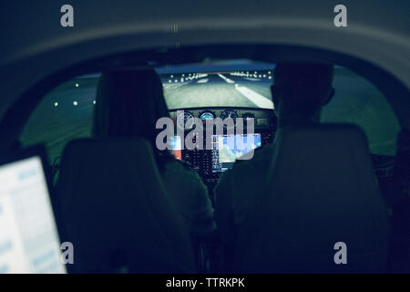 Rear view of silhouette pilot giving training to male trainee in flight simulator Stock Photo