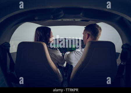 Rear view of male pilot guiding female trainee in flight simulator Stock Photo