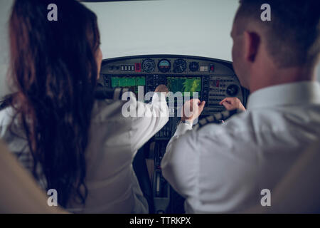 Rear view of male pilot guiding female trainee in flying flight simulator Stock Photo