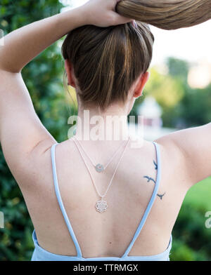 Rear view of woman wearing sleeveless top tying hair while standing outdoors Stock Photo