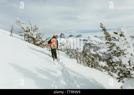 Rear view of hiker with backpack using ski poles while walking on snowcapped mountain Stock Photo