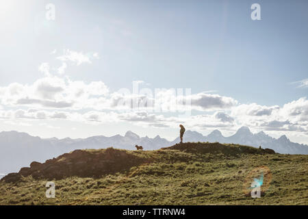 Silhouette male hiker with dog standing on mountain against sky during sunny day Stock Photo