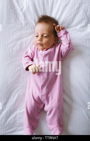 newborn baby girl in pink striped onesie lays on duvet bed Stock Photo