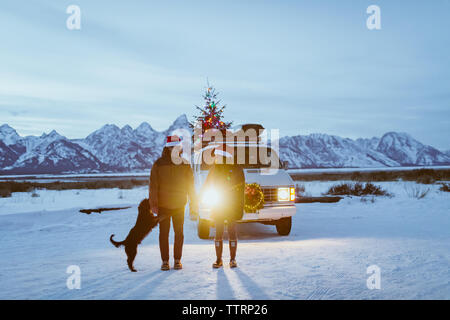 Dog jumps on couple holding hands in front of headlights Stock Photo