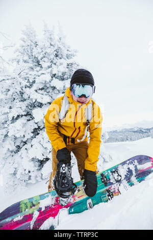 young man snowboarder in yellow jacket adjusts his board Stock Photo