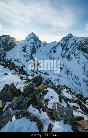 ridge top view of setting sun over snow covered rocky mountains Stock Photo