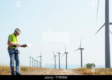Engineer reading documents at wind farm against sky Stock Photo