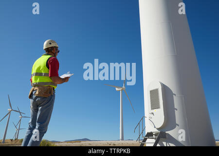 Low angle view of engineer holding clipboard while standing by windmills against sky Stock Photo