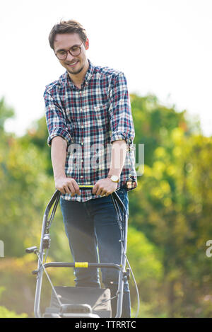 Happy man mowing at yard against clear sky during sunny day Stock Photo