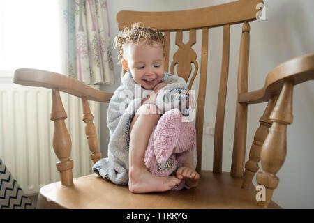Girl wrapped in towel sitting on chair at home Stock Photo