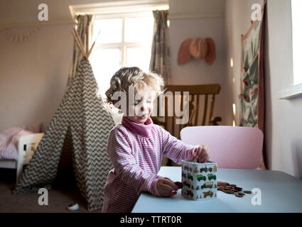 Girl putting coins in piggy bank while standing by table at home Stock Photo