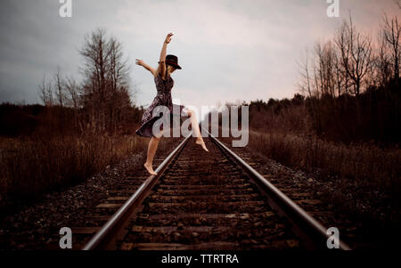Happy woman dancing on railroad tracks against cloudy sky during sunset Stock Photo