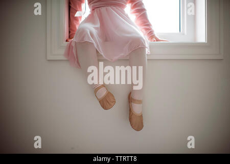 Low section of girl in ballet costume sitting on window sill at home Stock Photo