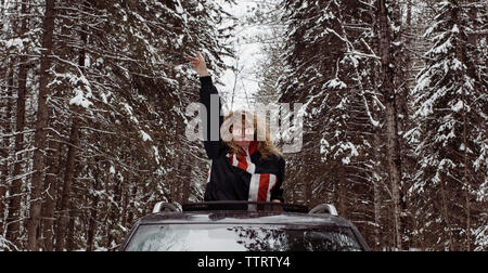Playful woman with arm raised blowing bubble gum while standing in car during winter Stock Photo