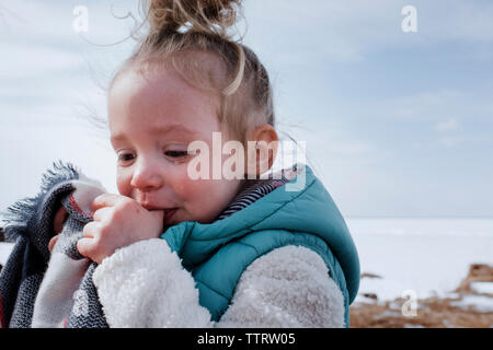 Close-up of crying girl sucking thumbs while standing against sky during winter Stock Photo