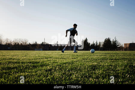 Man practicing soccer on grassy field against clear sky at park during sunset Stock Photo