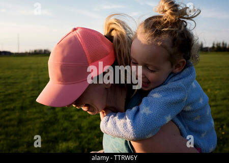 Close-up of happy mother piggybacking daughter while running at park against sky during sunset Stock Photo