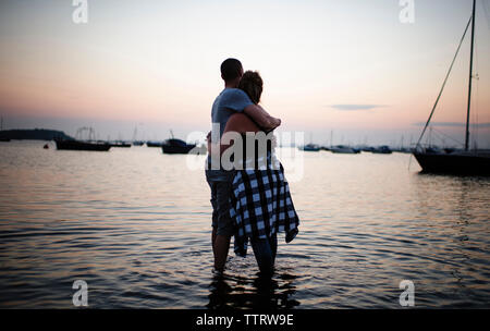 Couple embracing while standing in water against sky during sunset Stock Photo