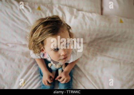 young blonde girl sat on her bed in her bedroom looking with toys Stock Photo