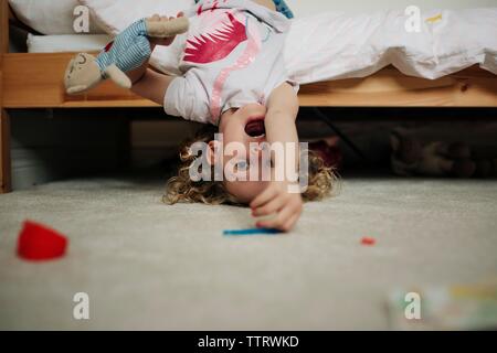 young blonde girl hanging upside down on bed smiling with soft toy