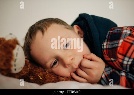 young blonde boy aged 6 laying down tired on his bed with teddy bear Stock Photo