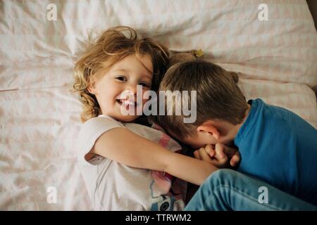 young girl looking up smiling and cuddling her brother at home Stock Photo