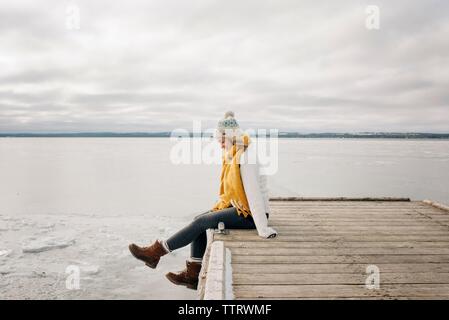 blonde woman sitting on the edge of a pier jetty smiling kicking feet Stock Photo