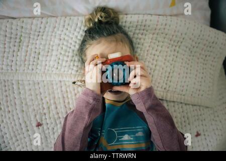 girl holding up camera to her face taking pictures playing in bedroom Stock Photo