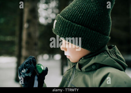 young boy looking at torch whilst standing in a snow covered forest Stock Photo