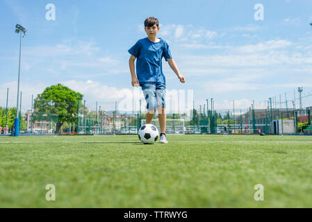 Low angle view of boy practicing soccer on field against sky Stock Photo