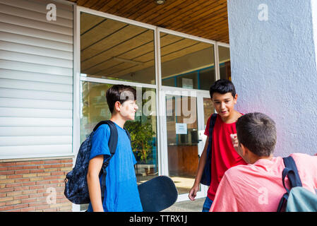 Friends with backpacks talking while standing against school building Stock Photo