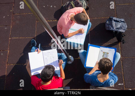 High angle view of friends studying while sitting on footpath during sunny day Stock Photo