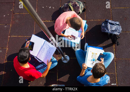 High angle view of friends using mobile phones while studying on footpath during sunny day Stock Photo