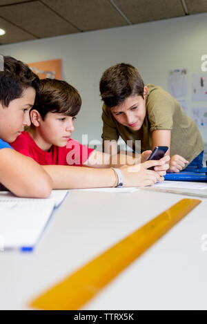 Friends looking at boy using smart phone in classroom Stock Photo