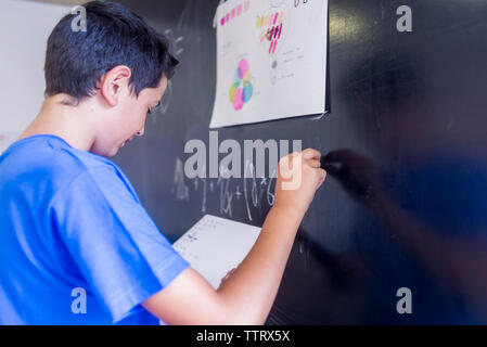 Side view of schoolboy writing on blackboard in classroom Stock Photo