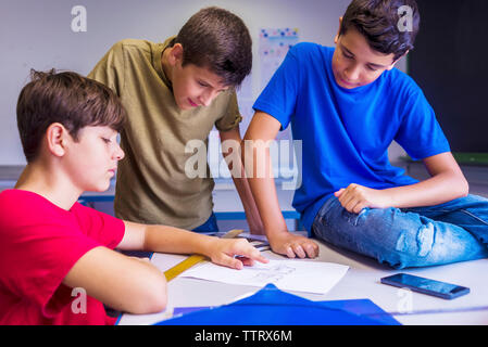 Schoolboys discussing paper in classroom Stock Photo