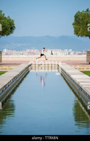Side view of man running on retaining wall against clear blue sky at park Stock Photo