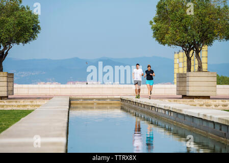 Couple running on retaining wall against clear blue sky at park Stock Photo