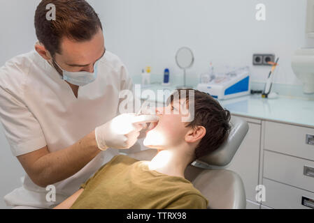 Dentist wearing surgical gloves and mask examining patient's mouth in medical clinic Stock Photo
