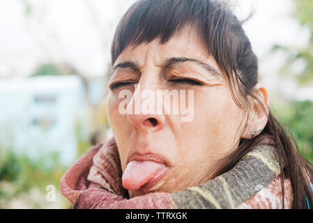 Portrait of woman eyes closed while sticking out tongue outdoors