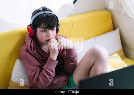 Above view of teen sitting on sofa with headphones looking laptop Stock Photo