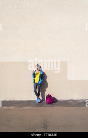 Young fit woman in sportswear leaning on wall while using phone Stock Photo