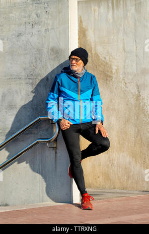 Senior man wearing sports clothes leaning on wall while looking away Stock Photo