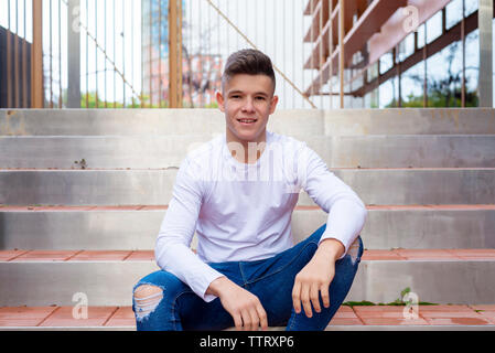 Front view of young man sitting on outdoors staircase, looking camera Stock Photo