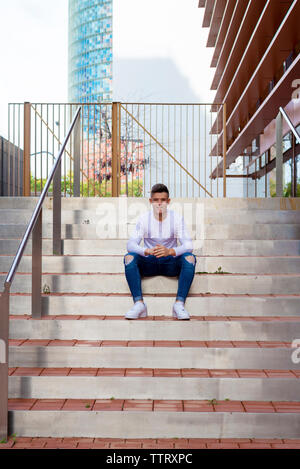 Front view of young man sitting on outdoors staircase, looking camera Stock Photo