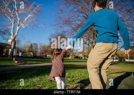 Rear view of daughter pulling father by holding his hands at park Stock Photo