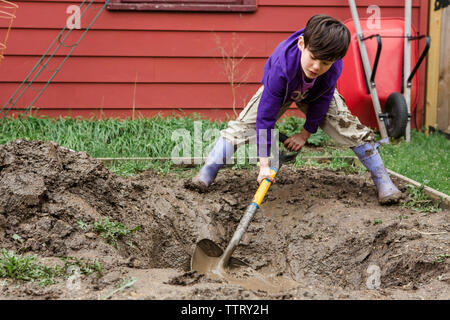 Full length of boy digging field with spade while gardening at backyard Stock Photo