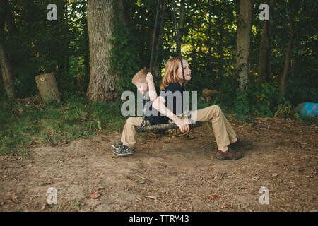 Brothers swinging on tire swing in forest Stock Photo